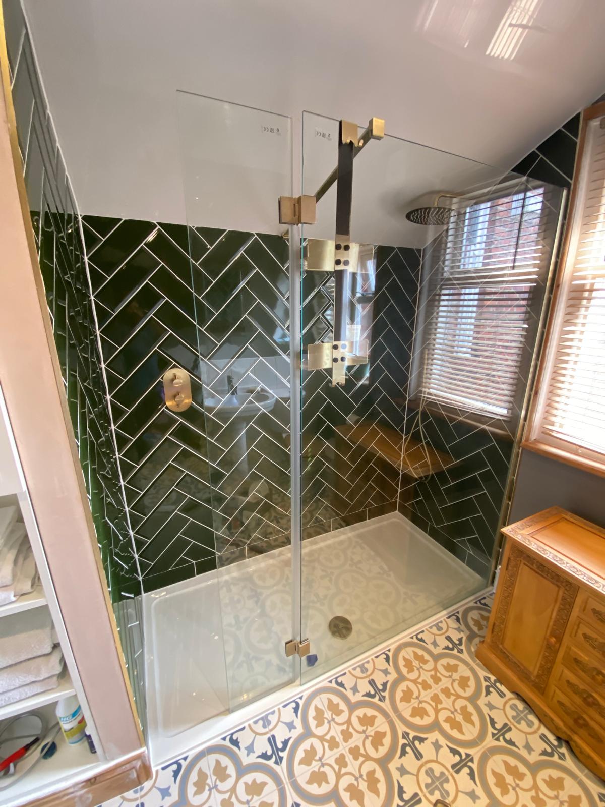 Finished shower with dark green herringbone tiling, frameless glass screen and brushed brass fittings