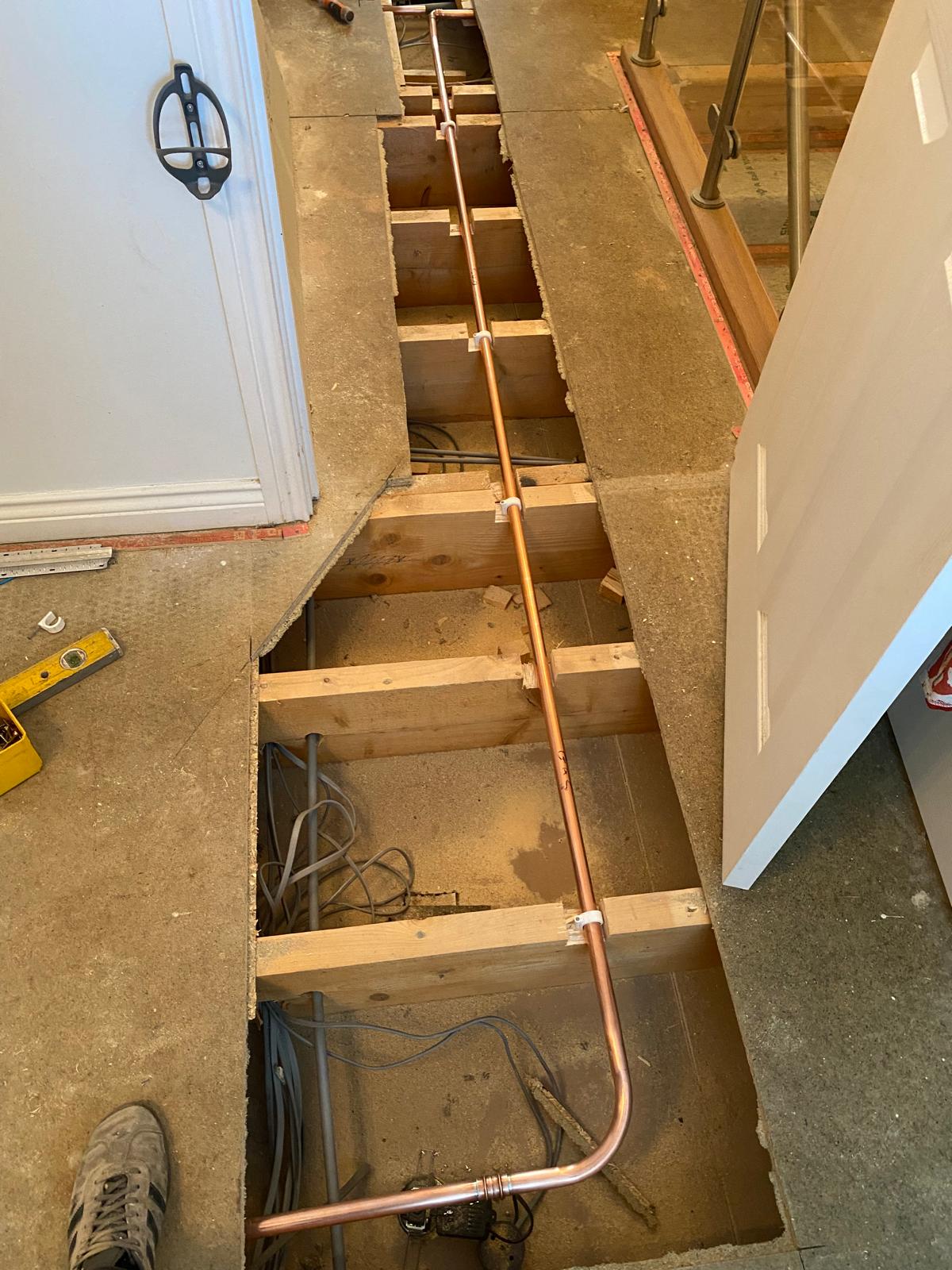 New copper gas pipe clipped through floor joists along a hallway