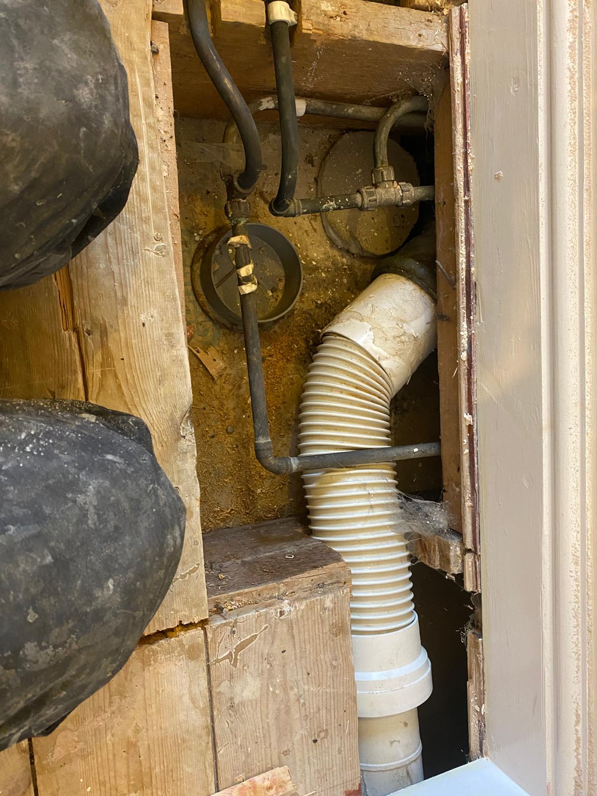 Old flexible waste pipe and loose fittings in a timber void before replacement