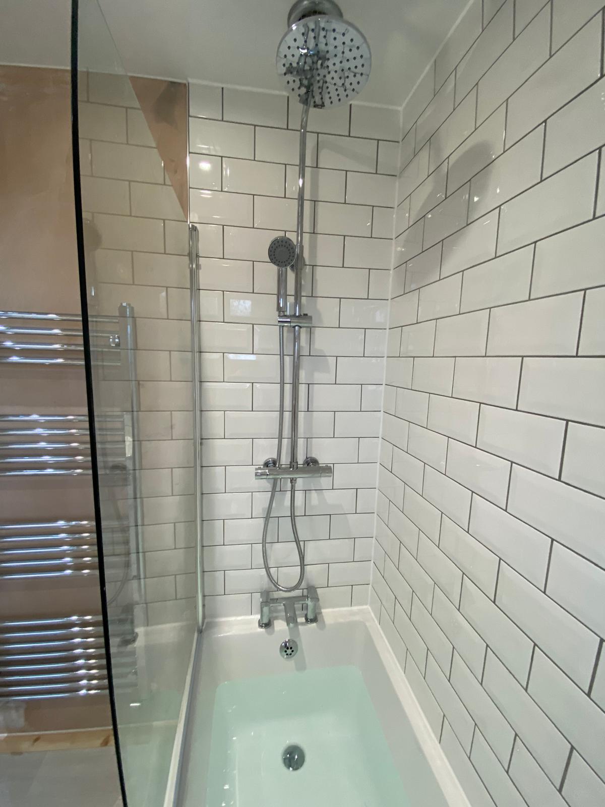 Bath with bar shower, handset and glass screen against white metro tiling with grey grout