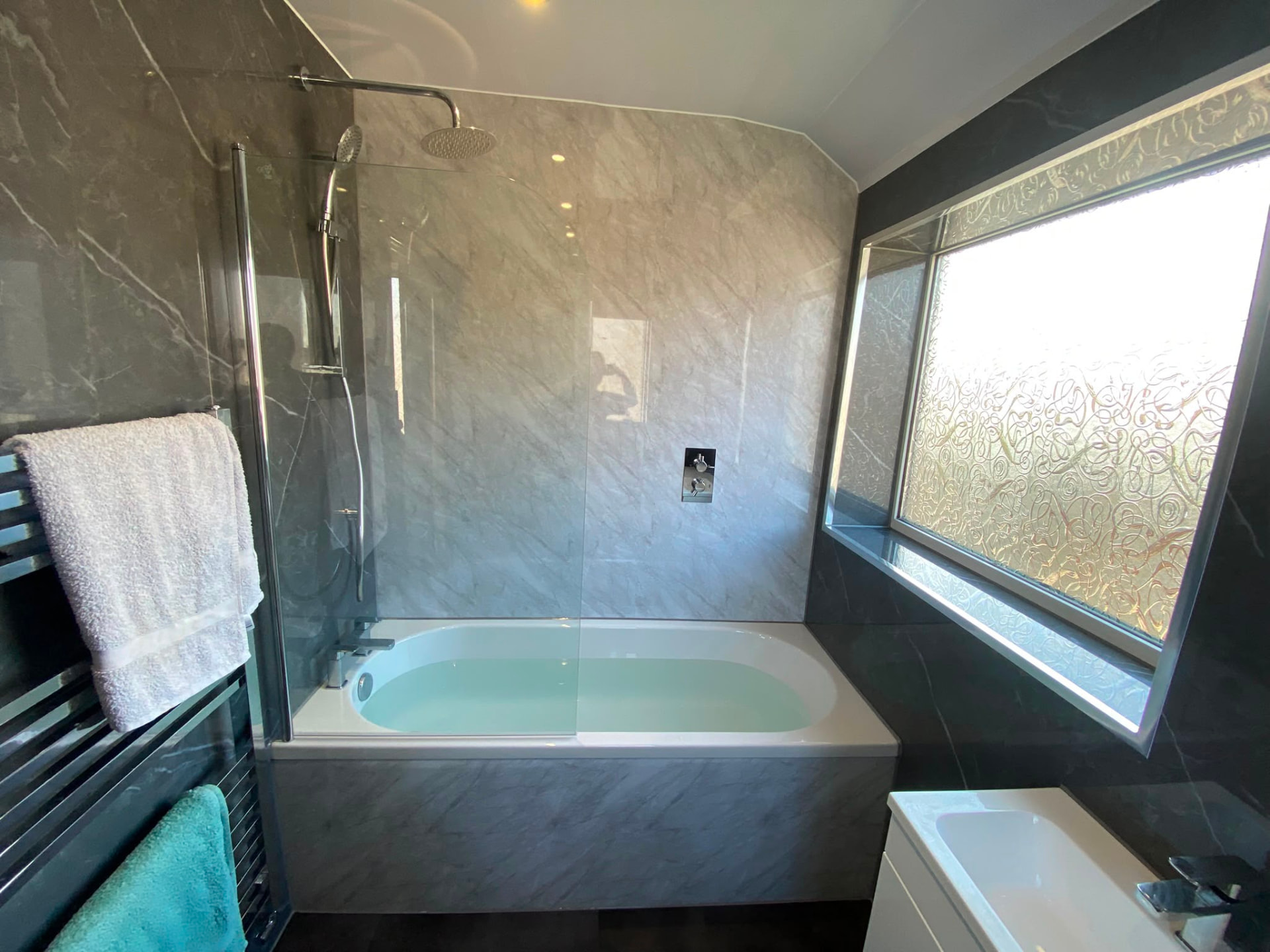 Bath with integrated mixer shower, glass screen and marble effect wet wall panelling in Bedlington Station