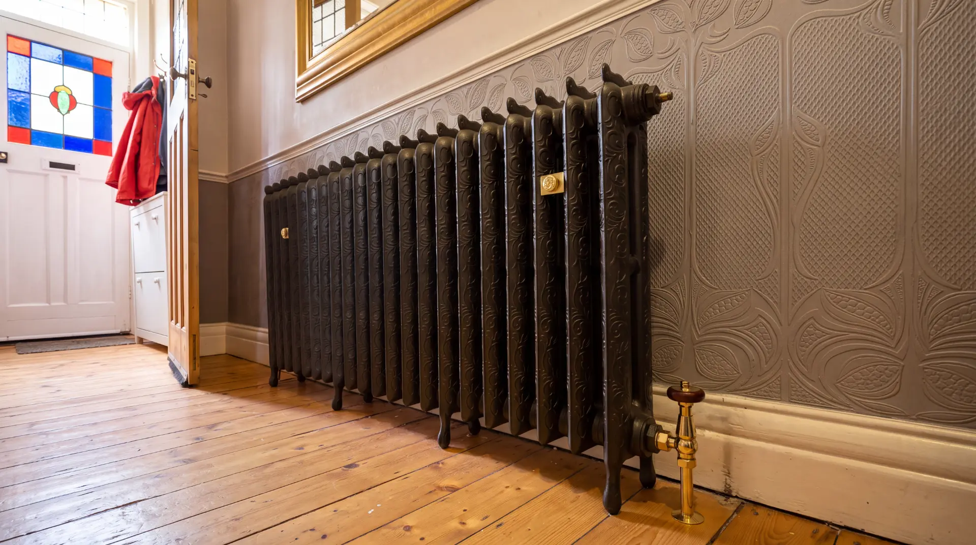 Ornate cast iron radiator with brass valves fitted in a period hallway