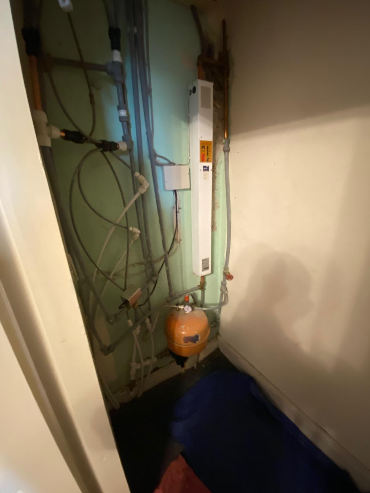 Old electric boiler with tangled plastic pipework and cables in a cupboard