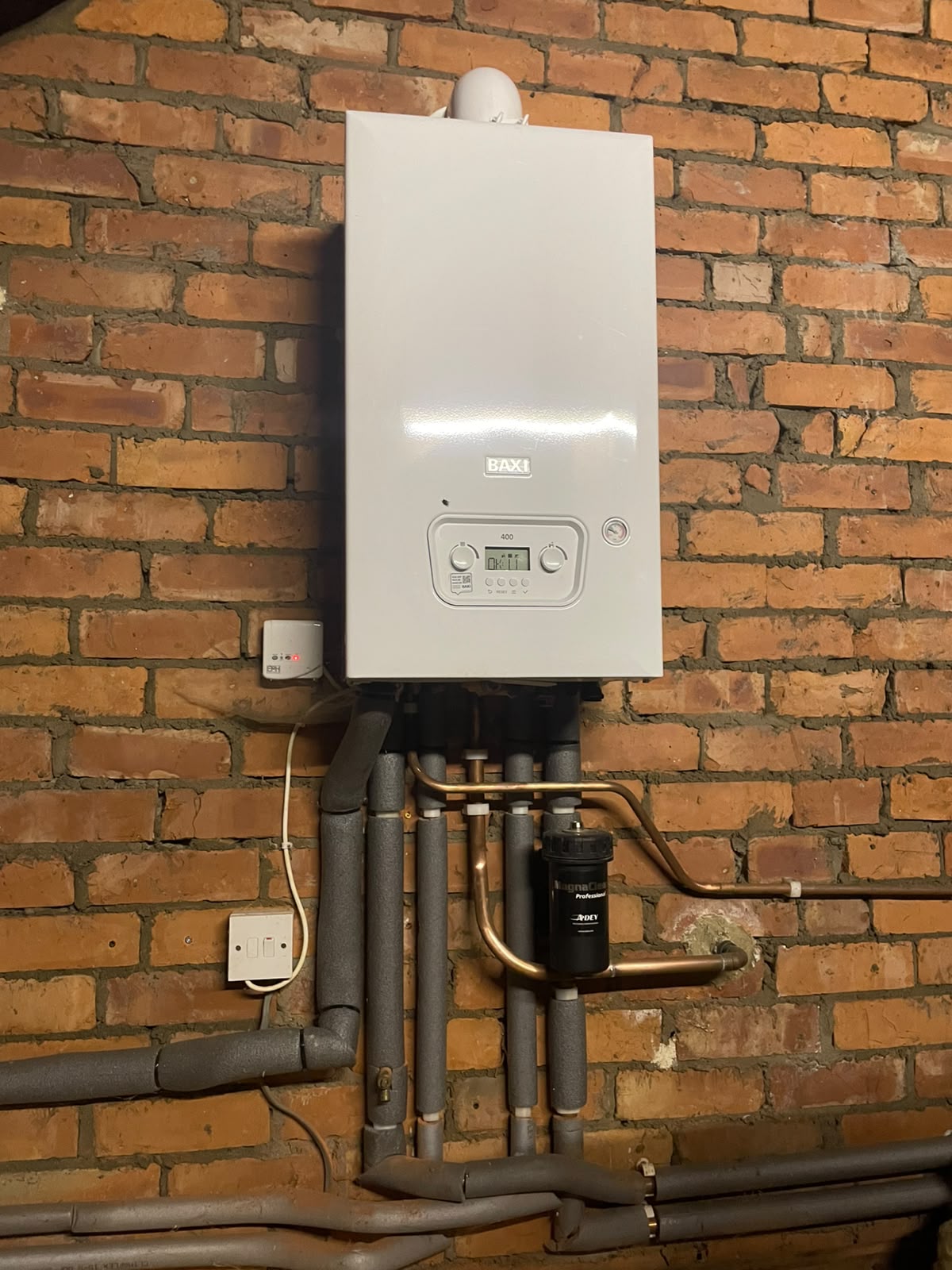New Baxi combi boiler installed on an exposed brick wall with neat copper and insulated pipework in a Bedlington loft