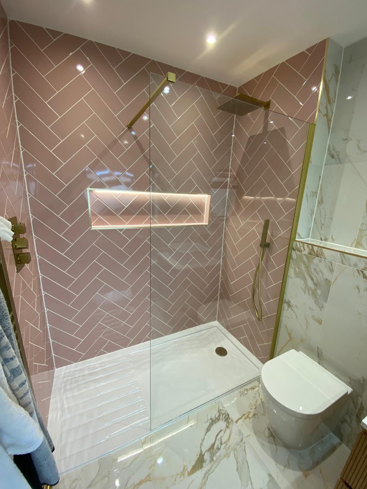 Walk-in shower with pink herringbone tiling, lit niche and brushed brass fittings