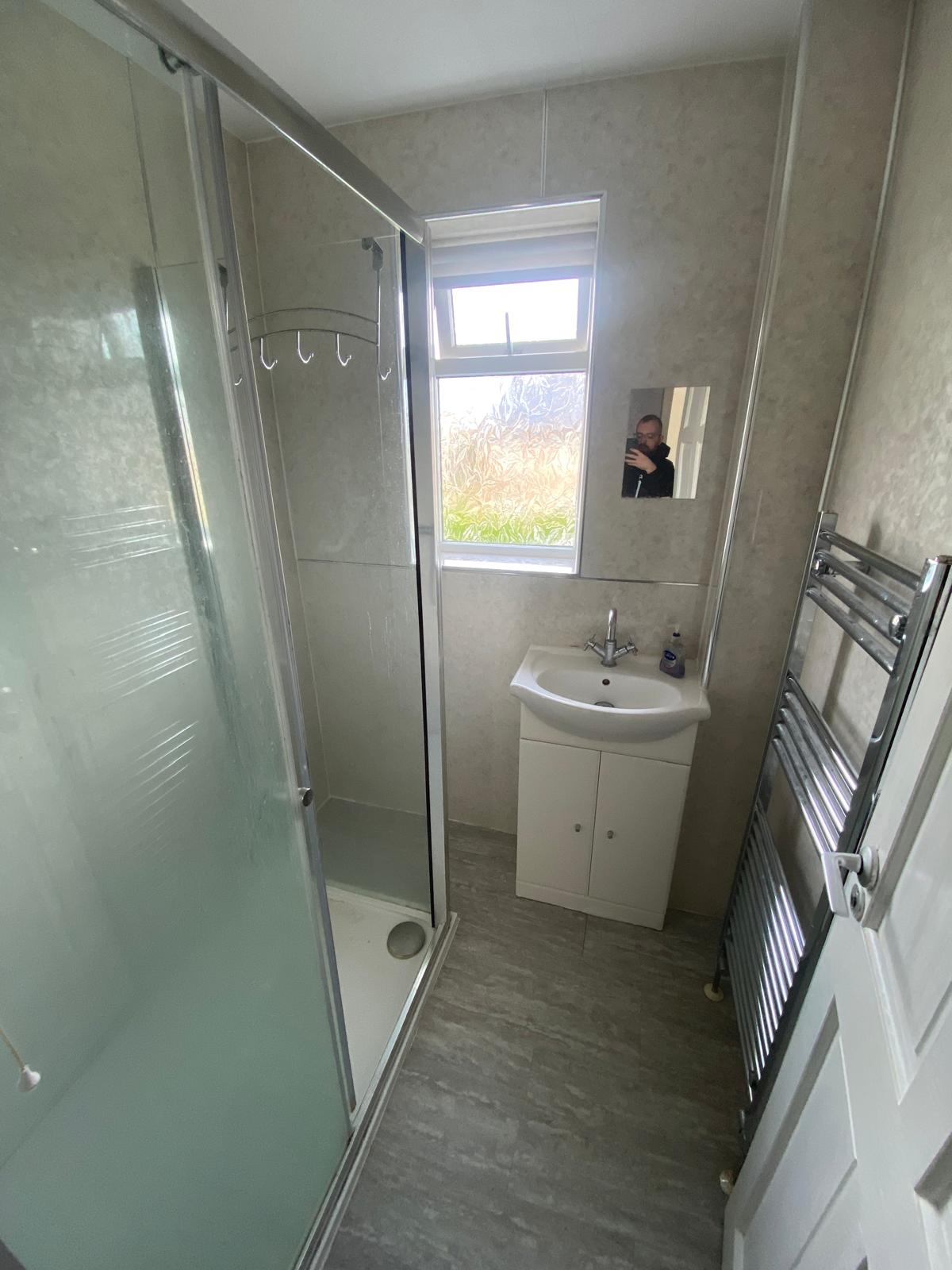 Original narrow shower room with corner cubicle, small basin unit and chrome towel rail