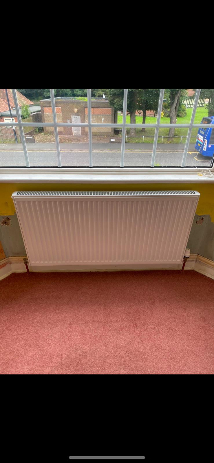 New white radiator fitted under a window on a finished heating system