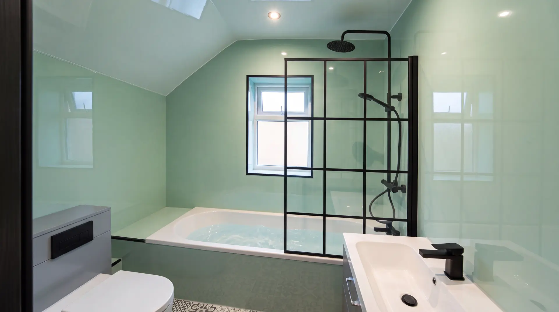 Finished bathroom with a bath, black framed shower screen and pale green wall panelling