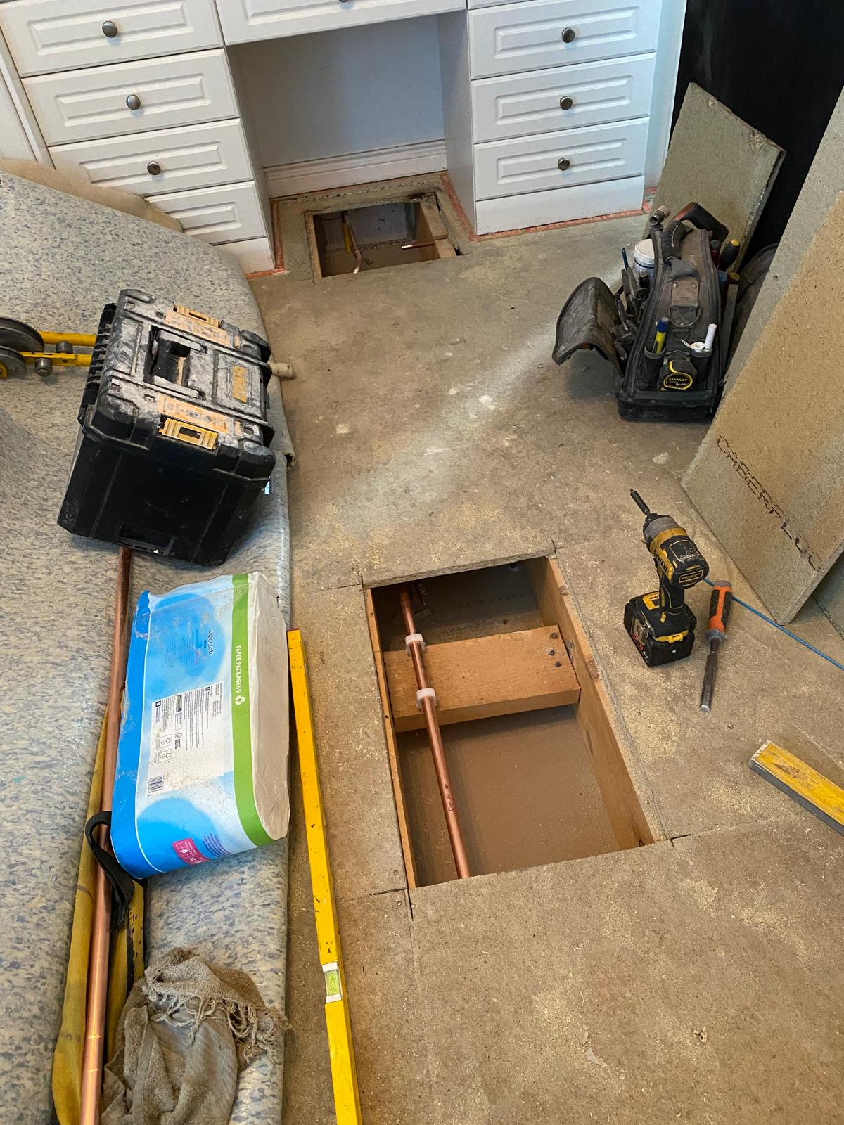 Floor boards lifted in a kitchen showing copper gas pipe being run between joists