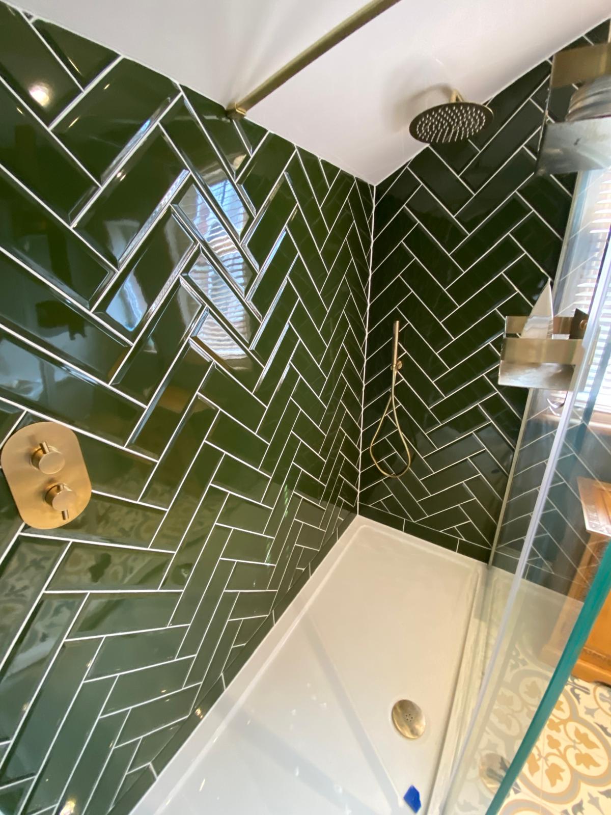 Close up of the dark green herringbone tiling with brushed brass rain head and thermostatic valve
