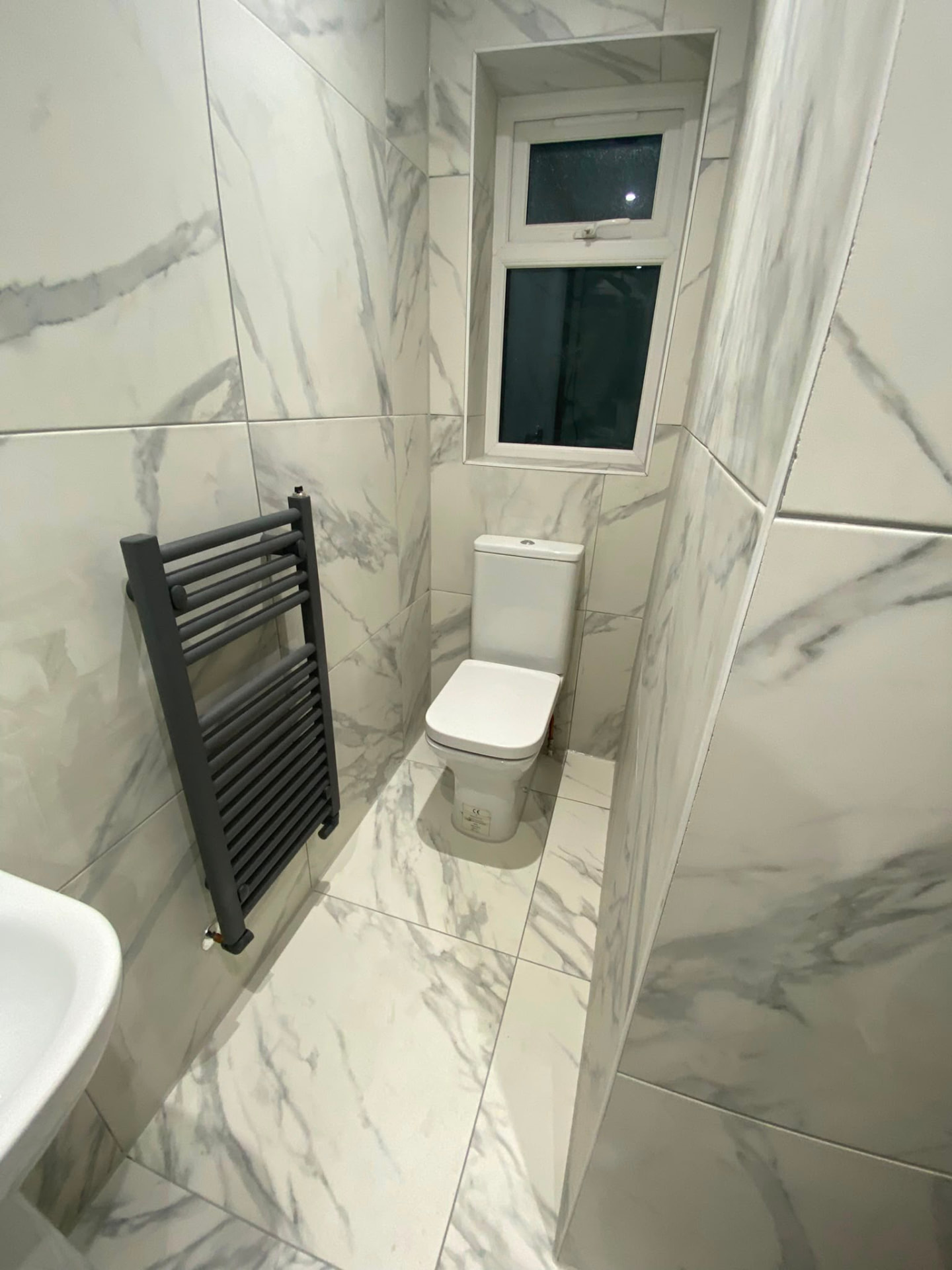 Bedlington bathroom with marble-effect tiles, wall hung WC and matt black towel rail