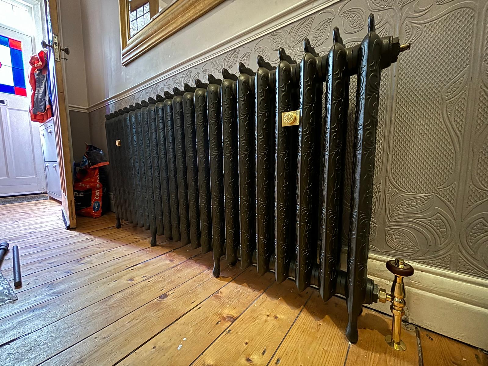 Ornate cast iron radiator on floor feet with brass valves in a period hallway