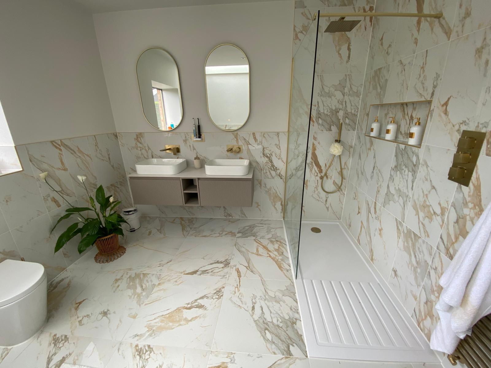 Twin basins on a wall hung vanity with brushed brass taps beside a walk-in shower