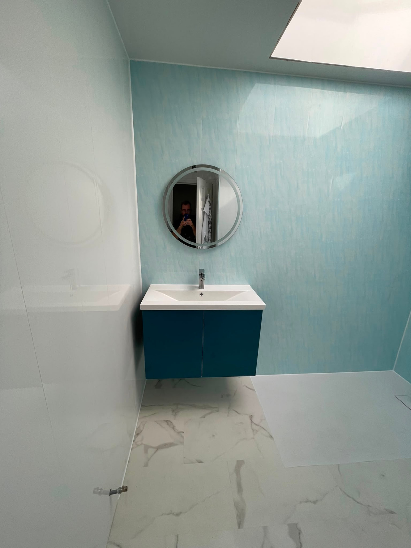 Wall hung teal vanity unit and round mirror in the finished wet room