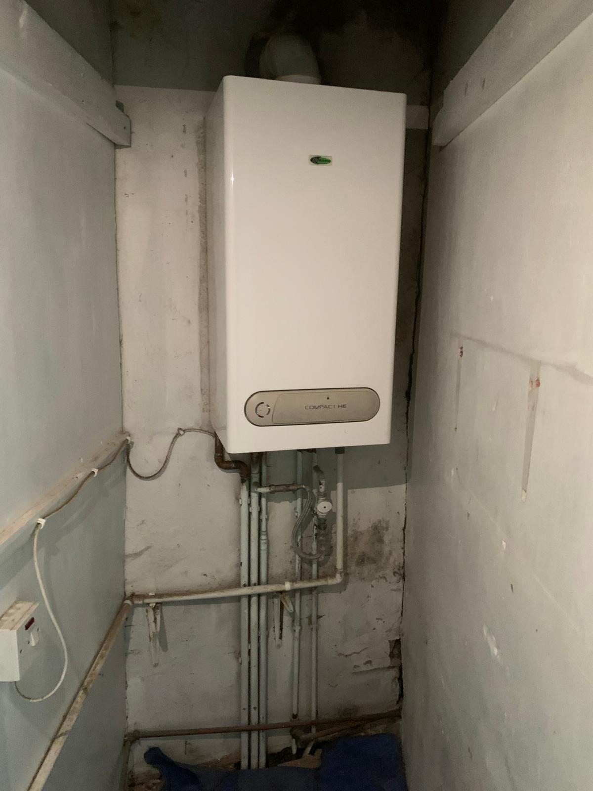 Old combi boiler in a cupboard with untidy pipework before replacement