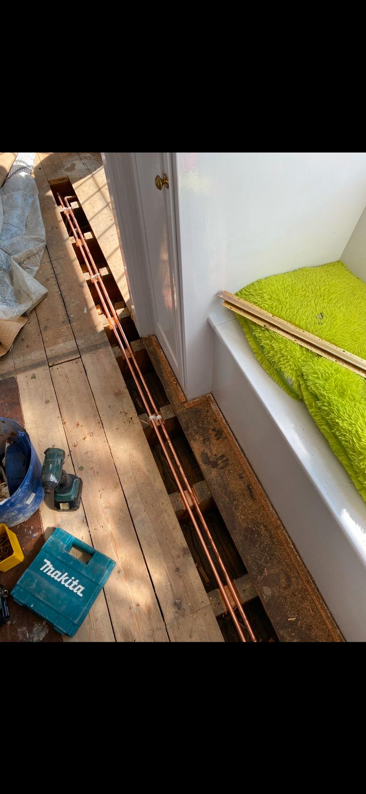New copper heating pipework run between floor joists with boards lifted