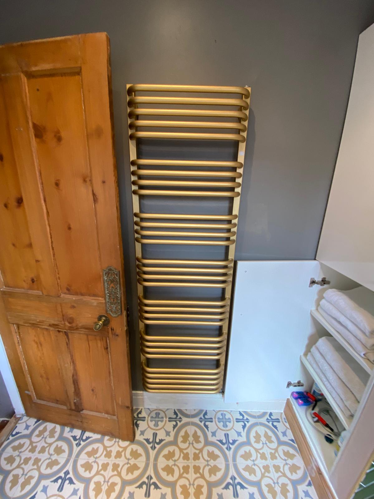 Brushed brass designer towel rail fitted in a bathroom with patterned floor tiles