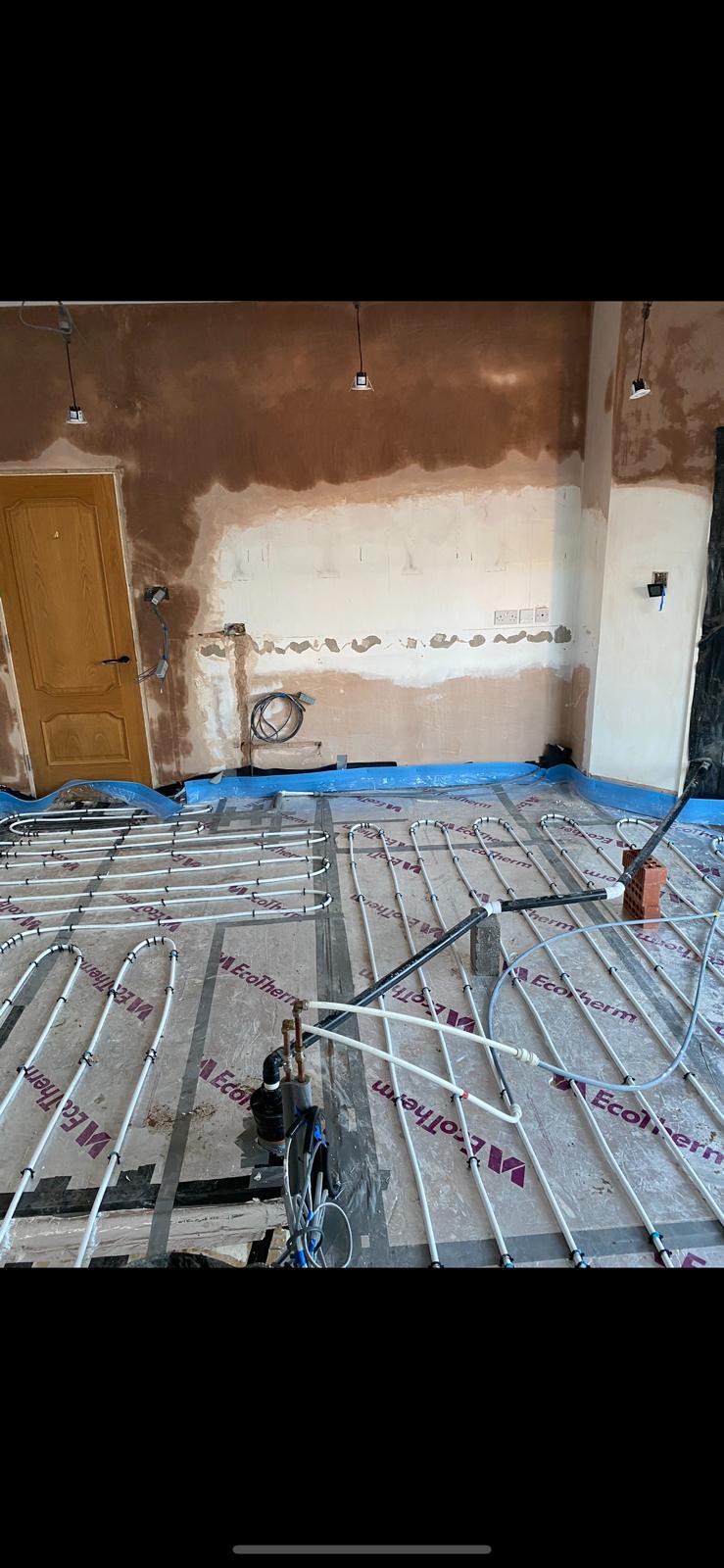 Downstairs room with radiators removed and underfloor heating loops clipped over insulation boards
