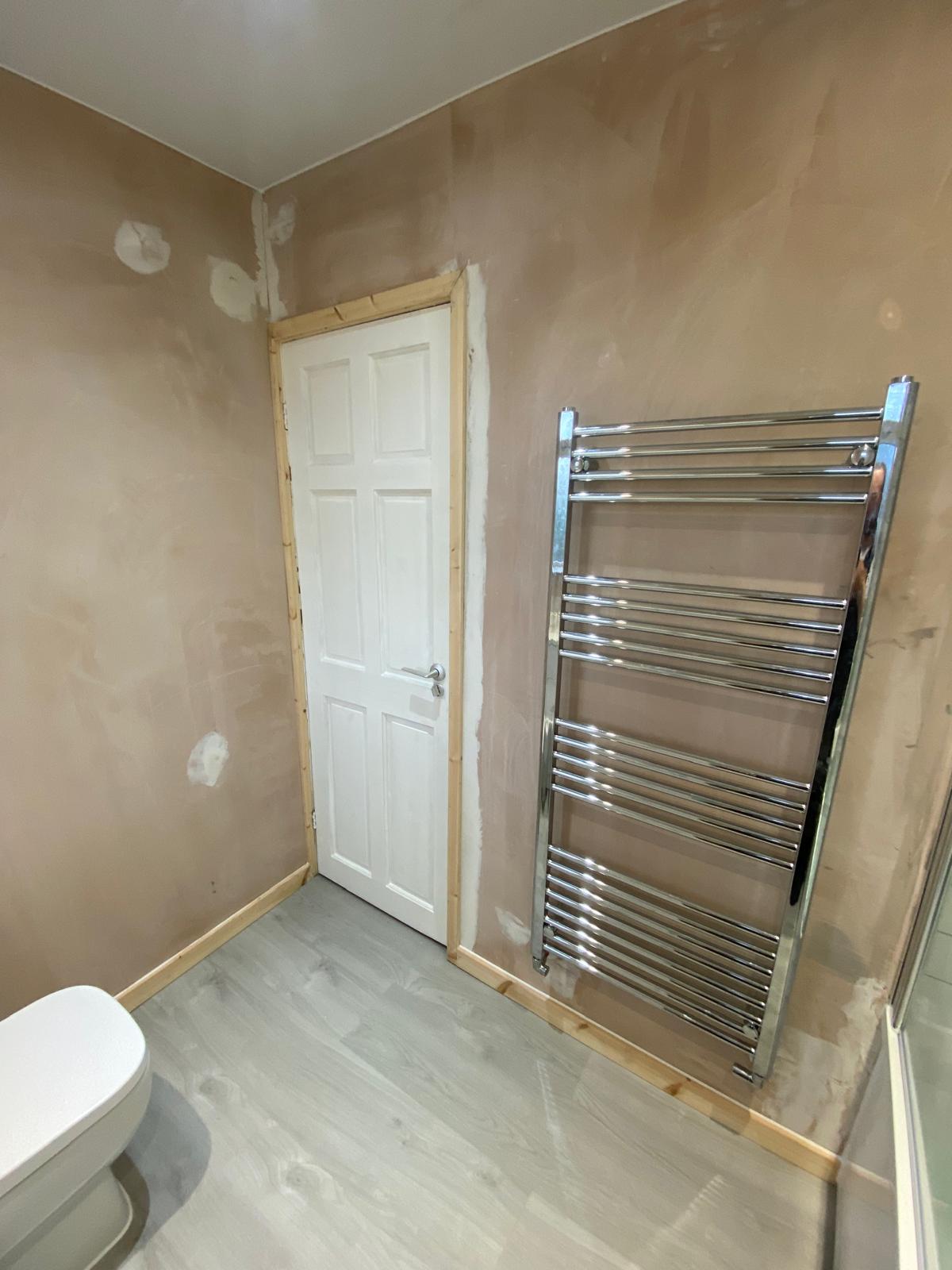 Chrome ladder towel rail fitted on the wall beside the bathroom door