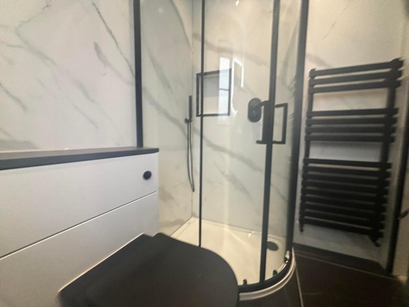 Quadrant shower enclosure with black frame and anthracite towel rail in a marble effect en-suite
