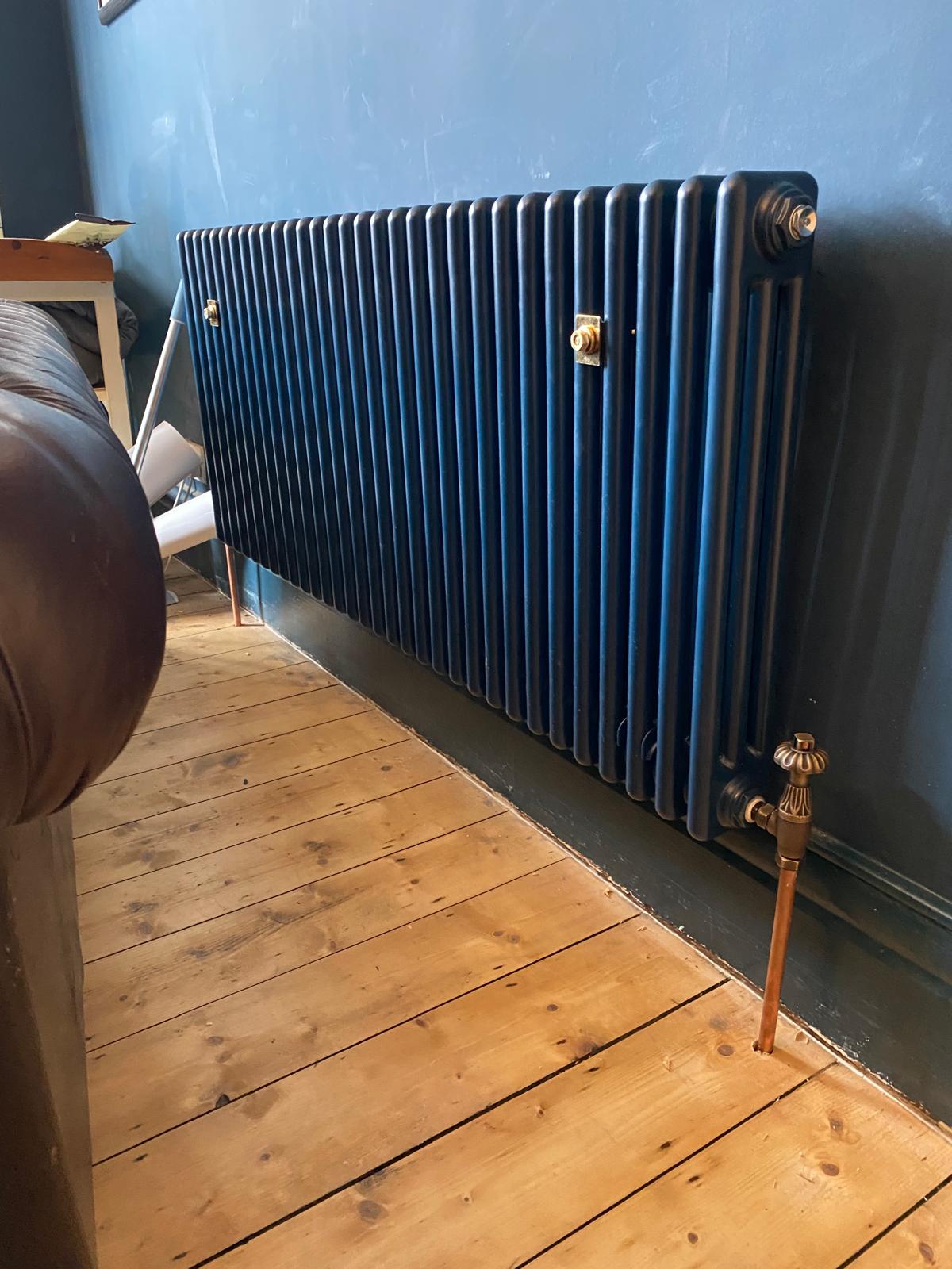 Horizontal navy column radiator with antique brass valves on stripped floorboards