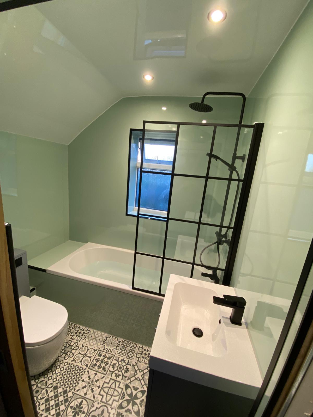 Finished bathroom with sage cladding, black grid shower screen and patterned floor tiles