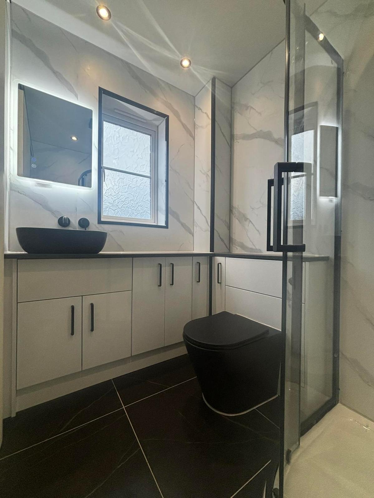 Finished en-suite with marble effect wet wall, black counter top basin and reused white units