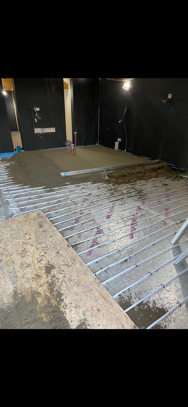 Screed being poured and levelled over the underfloor heating pipe loops