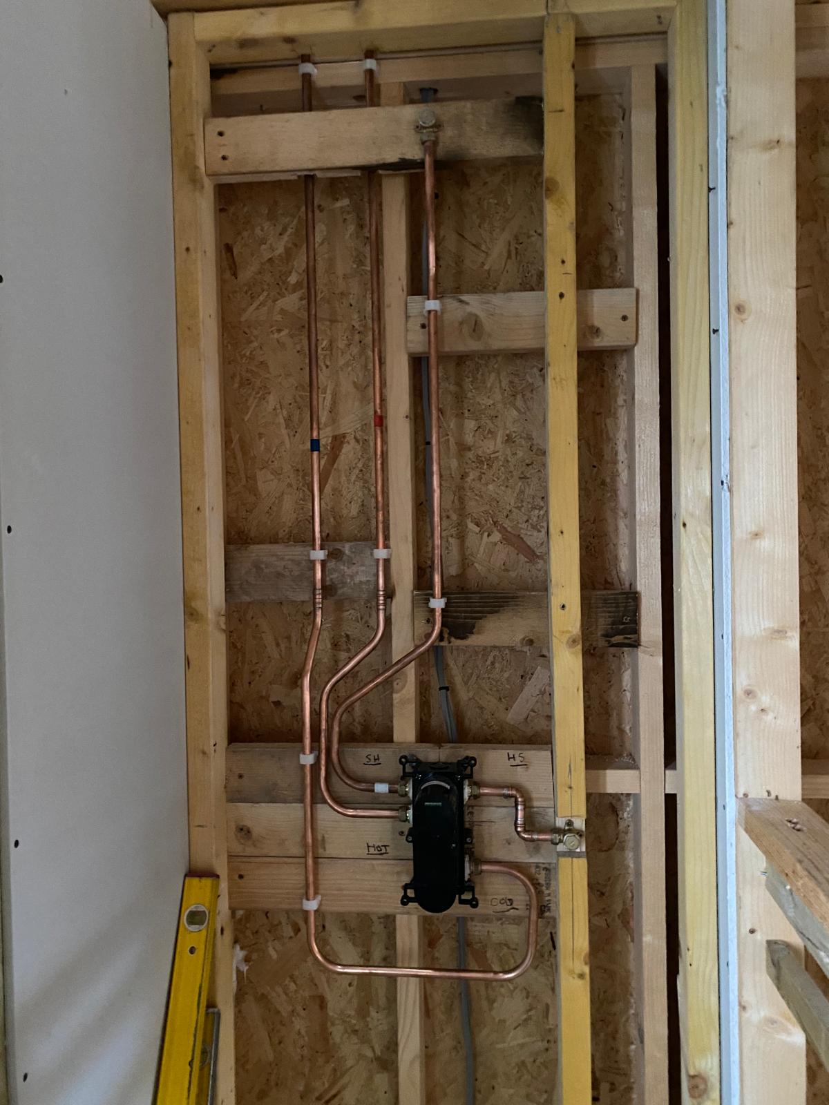 Copper hot and cold pipework and a shower pump mounted in a timber stud wall before boarding