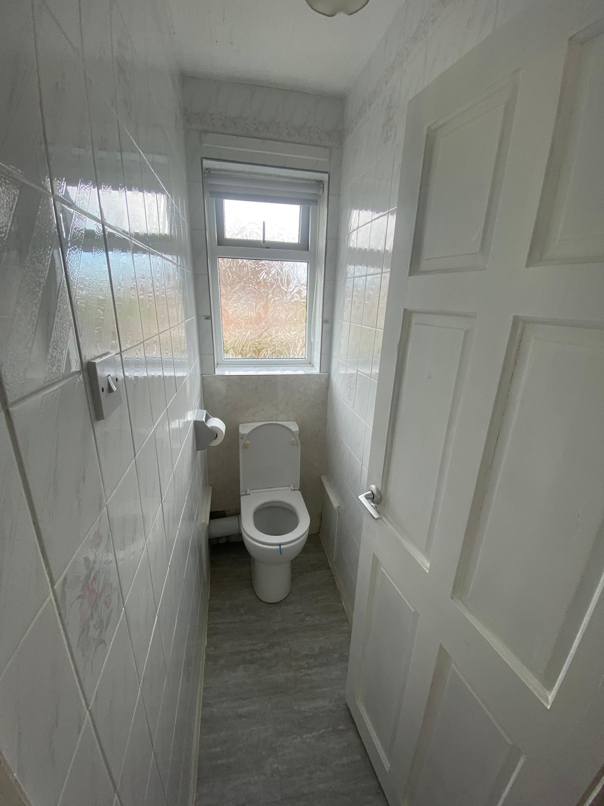 Original separate WC with dated white tiling and a close coupled toilet under the window