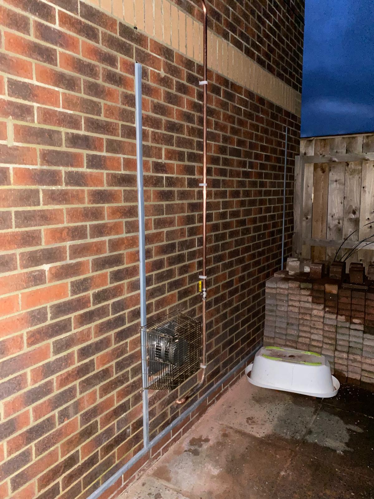 External copper gas pipework with isolation valve and label clipped to a brick wall