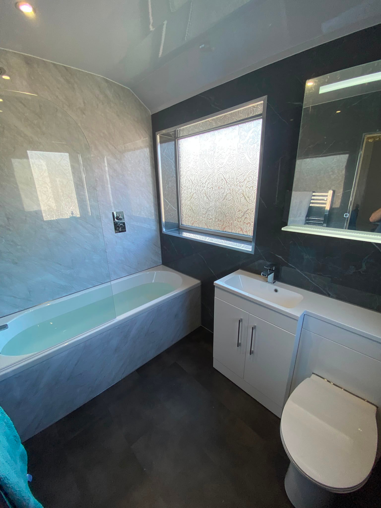 Bathroom in Bedlington Station clad in grey marble effect wet wall panels with a bath and shower screen
